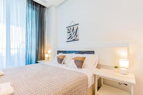 a white bedroom with a bed and a window at GEMELOS sea view apartment in Benidorm