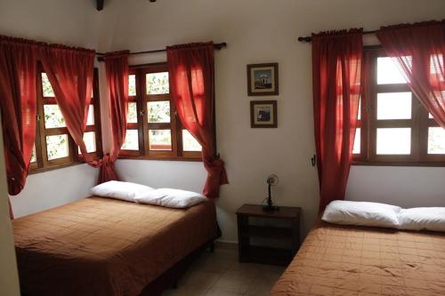 a bedroom with two beds and red curtains and windows at Hotel y Jardines Casa Búho in Antigua Guatemala