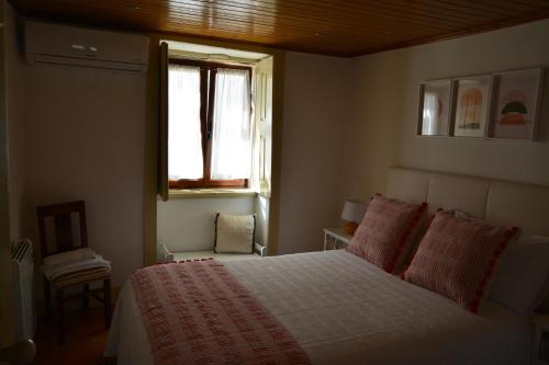 a bedroom with a bed with red pillows and a window at Casa do Alfaiate in Chãos