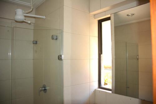 a bathroom with a shower with a mirror and a window at Apto Romântico frente mar vista mar Elegance Flat in Natal
