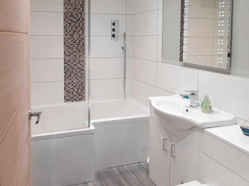a white bathroom with a shower and a sink at Beach Cottage in Benllech