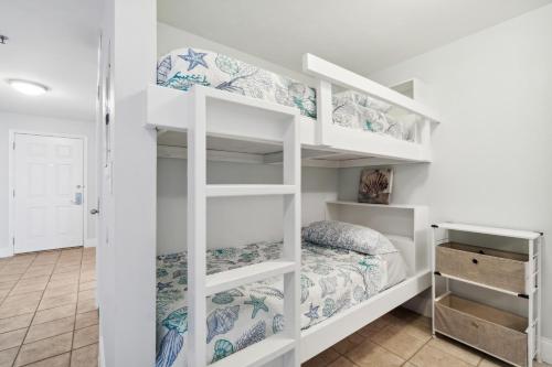 a bedroom with white bunk beds with a bed at Spacious Resort Condo with Breathtaking Gulf Views! by Dolce Vita Getaways PCB in Panama City Beach