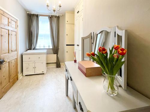 baño con jarrón de tulipanes y espejo en Wisteria Cottage, en Uppingham