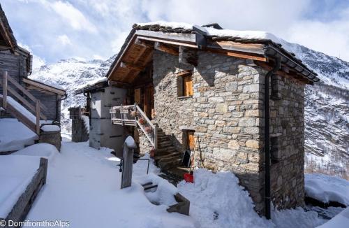 a stone building in the snow with mountains in the background at Haus Zer Trächu in Saas-Almagell