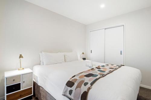 a white bedroom with a bed and a night stand at FERNZ Motel & Apartments Birkenhead in Auckland