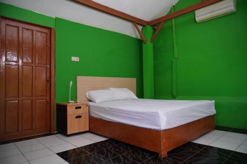 a green bedroom with a bed and a wooden door at Omah Bogem Homestay Syariah in Randugunting