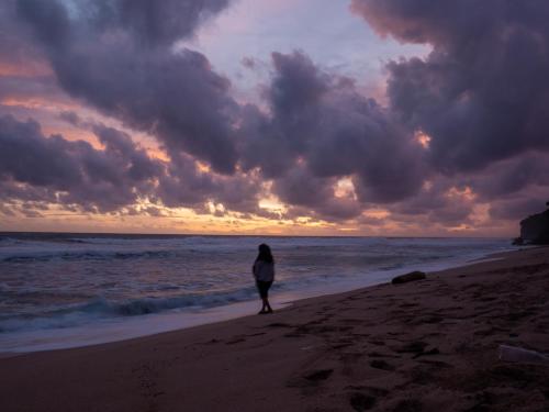 a woman walking on the beach at sunset at Villa Watu kodok - Villa Located Close to The Beach in Baron