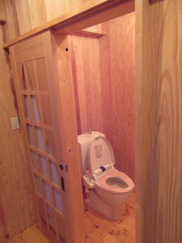 La salle de bains est pourvue de toilettes et d'un mur en bois. dans l'établissement 民泊くま - 絵画と音楽の宿, à Inawashiro