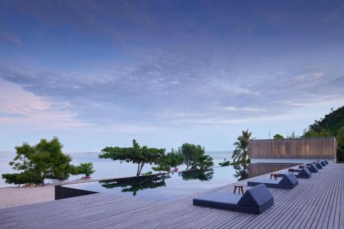 a row of lounge chairs sitting on a deck near the ocean at Innit Lombok in Ekas