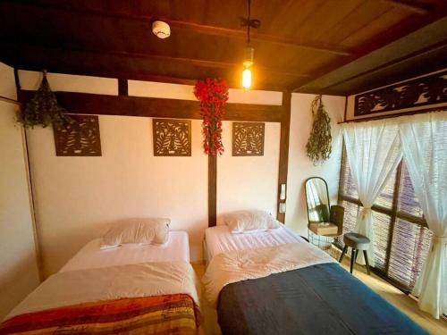 2 camas en una habitación con 2 ventanas en 一棟貸し切り バリの雰囲気を楽しめる古民家vintagehouse1925Bali, en Nagano
