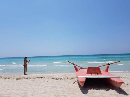 a woman standing next to a red boat on the beach at casa Pumi nel centro storico di Nardo' con terrazza panoramica in Nardò