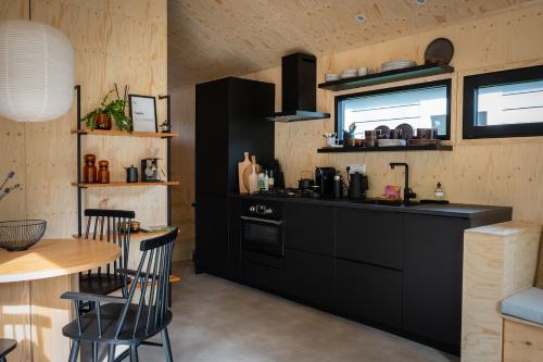 a kitchen with black cabinets and a table and a counter at Vague Luxurious Tiny House Luxe Wellness, Spa Bad,Beamer, Veluwe in Nunspeet