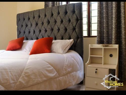 Khalisee Homes Studio Apartment 2 في Voi: غرفة نوم بسرير كبير مع شراشف بيضاء ومخدات برتقالية