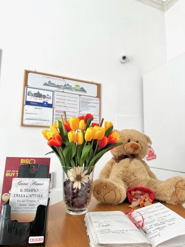 a teddy bear sitting on a desk with a vase of flowers at Il Tempio Della Capitale in Rome
