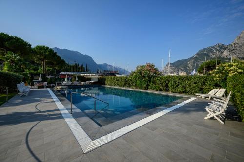 a swimming pool with two chairs and mountains in the background at Hotel Riviera in Riva del Garda