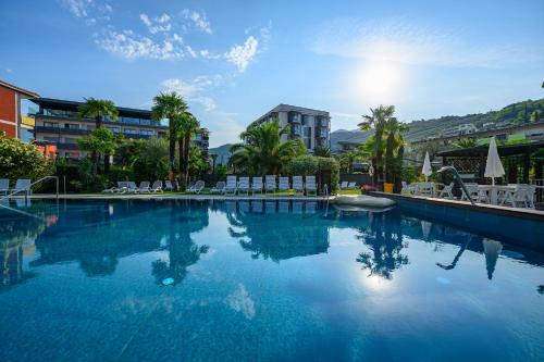 a large swimming pool with chairs and trees and buildings at Hotel Riviera in Riva del Garda