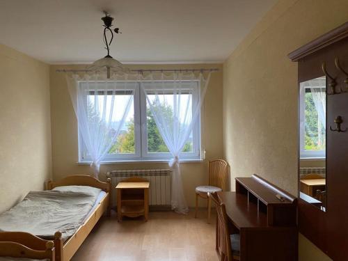 a bedroom with a bed and a desk and two windows at Willa Koniaków in Koniaków