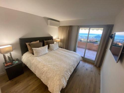 une chambre avec un grand lit et une grande fenêtre dans l'établissement Appartement avec vue mer panoramique, à Mandelieu-la-Napoule