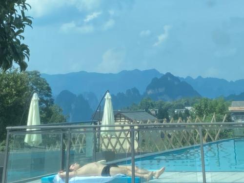 a person laying in a swimming pool with mountains in the background at Zhangjiajie National Park Nvue Resorts in Zhangjiajie