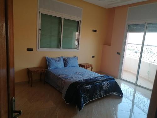 Schlafzimmer mit einem Bett mit blauer Bettwäsche und einem Fenster in der Unterkunft Appart el bassatine pr famille in Meknès