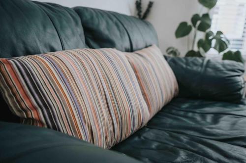 a striped pillow on a black leather couch at Orange Rentals - In my 4 bedroom Liverpool Home in Liverpool