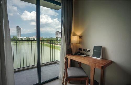 Habitación con escritorio y balcón con ventana. en Brique Suite, en Chiang Mai