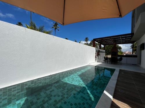 a swimming pool next to a white wall with an umbrella at Casa Maragogi, Piscina, 4 Suítes, 100 Mts Praia in Maragogi