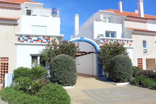 a white building with a blue door and some bushes at Carlota House - Baleal in Baleal