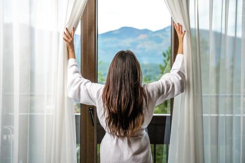 Una mujer abriendo una ventana con los brazos en alto. en Maxi Park Hotel & Spa, en Velingrad