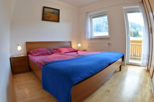 Schlafzimmer mit einem Bett mit blauer Bettwäsche und einem Fenster in der Unterkunft Apartments Rožič in Kranjska Gora