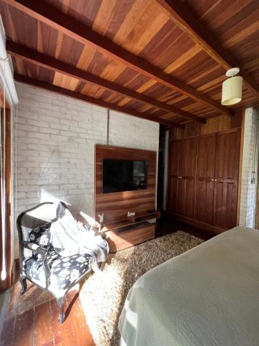 Schlafzimmer mit einem Bett, einem TV und einem Stuhl in der Unterkunft Chalés Vila Flor in Gonçalves