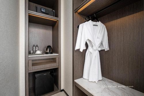 a white robe hanging on a wall in a bathroom at Cascade Hotel Bangkok in Bangkok