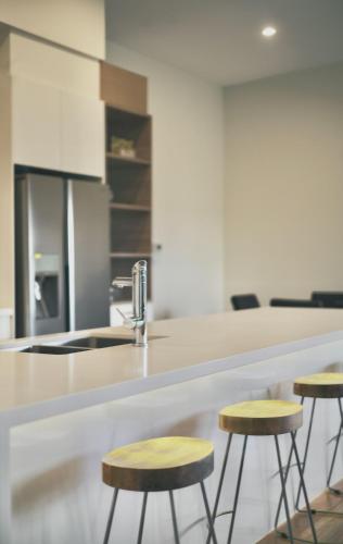 a kitchen with three bar stools and a sink at Pinecone Lodge - Luxury 4BR Home l EV Charger l Fire Pit l WiFi l BBQ l 4 Car Garage in Jindabyne