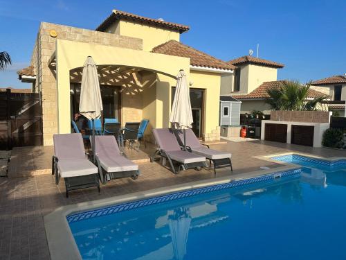 a swimming pool with chairs and umbrellas next to a house at Villa Kallista in Pissouri