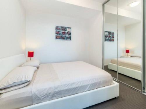a white bedroom with a large bed and a mirror at 806/67 Arvia in Newcastle