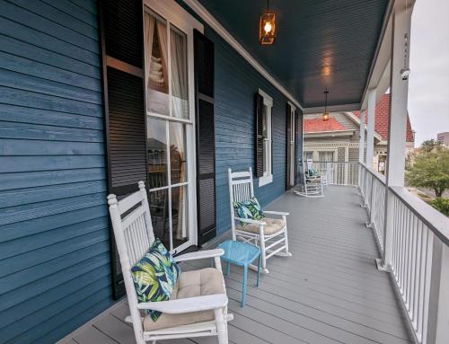 a porch of a blue house with two chairs at The 1890 Freeman House in Galveston
