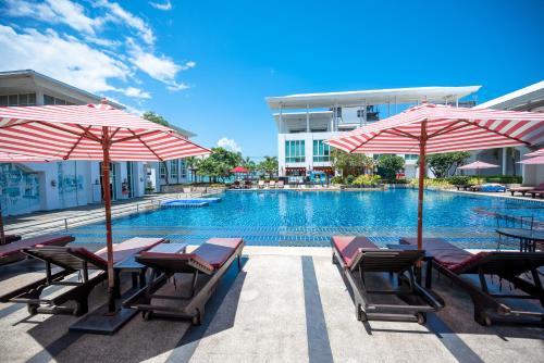 a pool with chairs and umbrellas next to a building at D Varee Jomtien Beach, Pattaya in Jomtien Beach