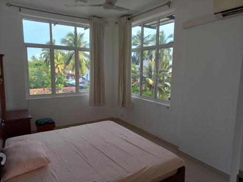 a bedroom with a bed and two windows with palm trees at The Anchorage Villa - Negombo in Negombo