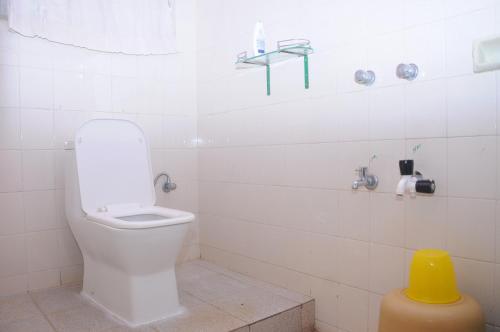 a white bathroom with a toilet and a yellow stool at Misty Retreat (Pragati House) in Madikeri