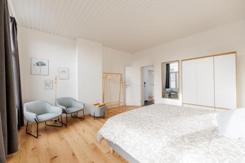 a white bedroom with a bed and two chairs at SurPRIMO - Gerenoveerd appartement in Antwerp