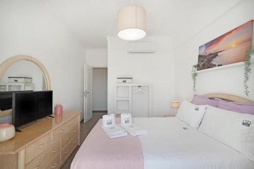 ein weißes Schlafzimmer mit einem großen Bett und einem TV in der Unterkunft Costa Beach Apartment by The Portuguese Butler in Costa da Caparica