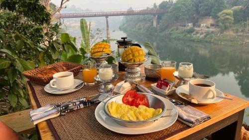 a table with a breakfast of fruit and coffee and a river at Moonlight Champa Riverview in Luang Prabang