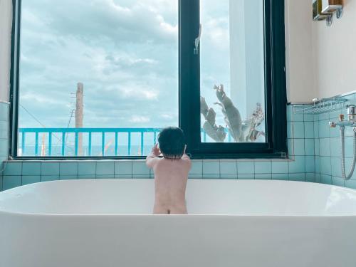 a baby sitting in a bath tub looking out a window at Lugo Hotel in Manzhou