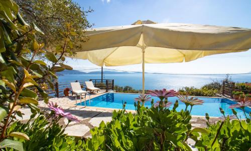 a pool with an umbrella and chairs and the ocean at The Lookout, boutique villa. in Sivota
