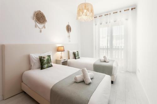 Habitación blanca con 2 camas y lámpara de araña. en Nazaré Modern Flat, en Nazaré