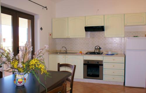 a kitchen with a table and a white refrigerator at Sa Fiorida Appartamenti in Valledoria