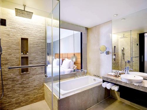 a bathroom with a tub and a bed and a sink at Pullman Bali Legian Beach in Legian