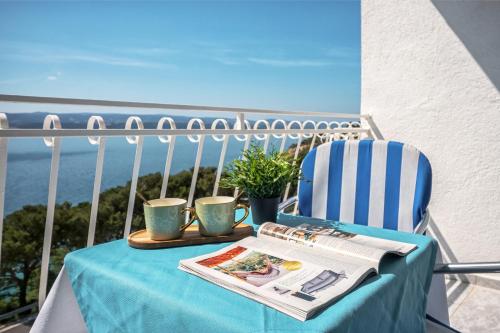 a table and a chair on a balcony with a newspaper at Skalinada Sea View in Lokva Rogoznica