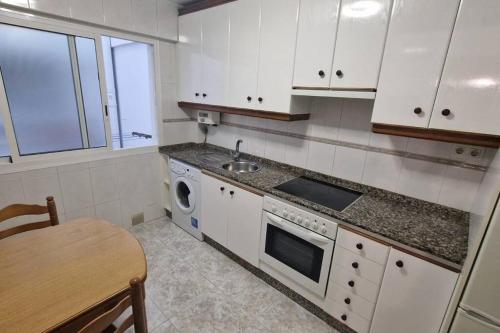 eine Küche mit weißen Schränken, einer Spüle und einem Tisch in der Unterkunft VibesCoruña- San Rosendo 25 in A Coruña
