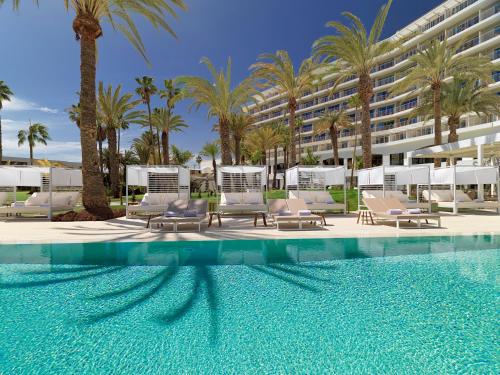 a pool with chairs and palm trees and a building at Paradisus by Meliá Gran Canaria - All Inclusive in San Agustin